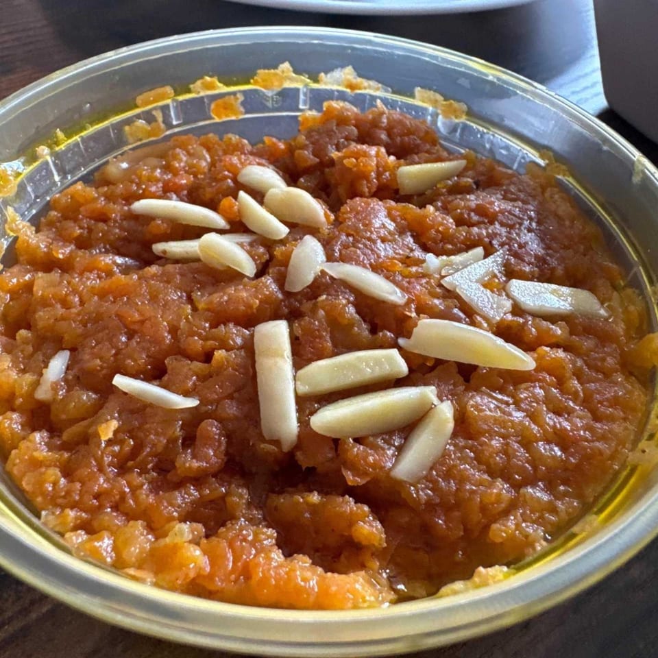 Aha South Indian Cuisine's orange Indian dessert, possibly halwa, topped with slivered almonds in a clear container.