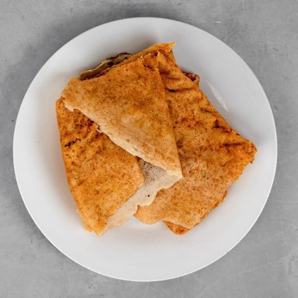 Three golden-brown dosas, folded and stacked on a white plate, against a gray background.
