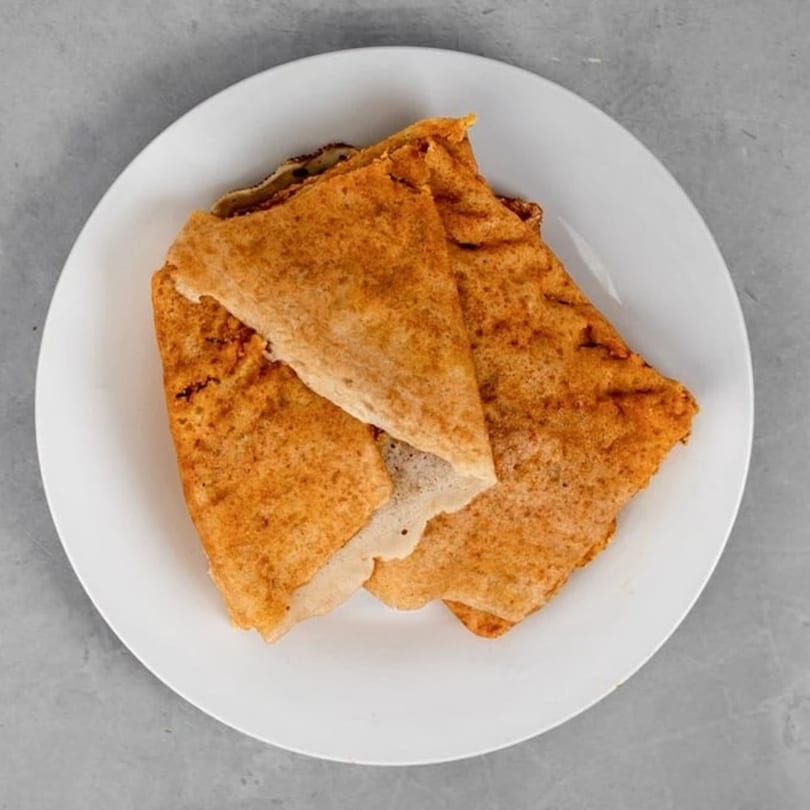 Three golden-brown dosas, folded and stacked on a white plate, against a gray background.