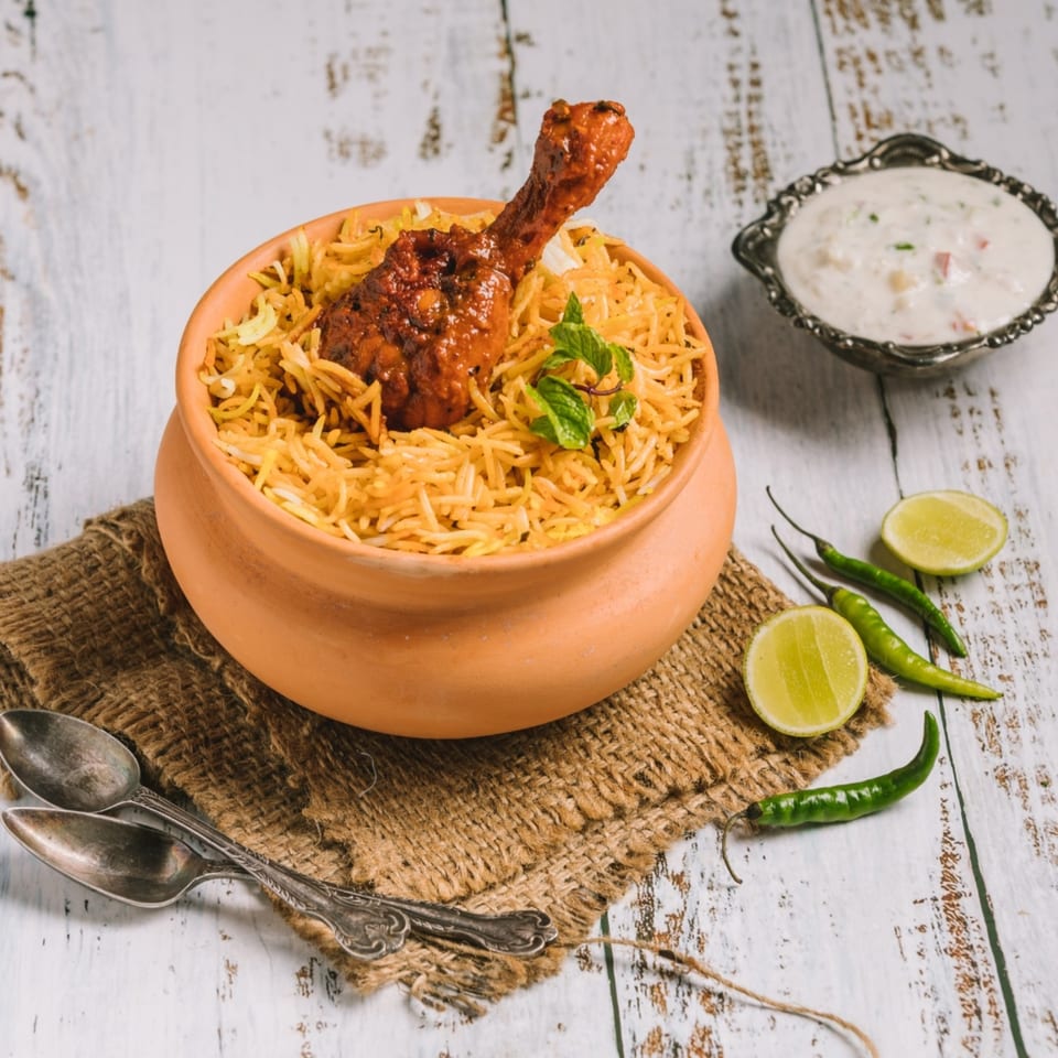 Aha South Indian Cuisine's chicken biryani in a clay pot with raita, lime, and chilies.