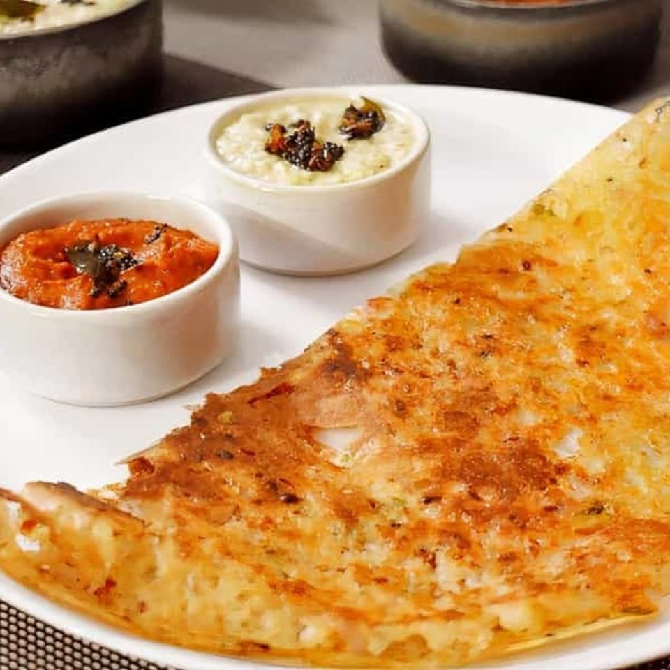 Crispy golden dosa with two small bowls of red and white chutneys on a white plate.