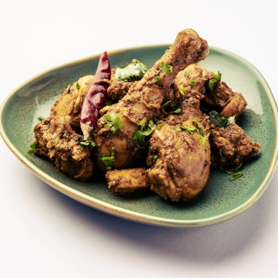 Aha South Indian Cuisine's chicken drumsticks and pieces, garnished with cilantro and a red chili.